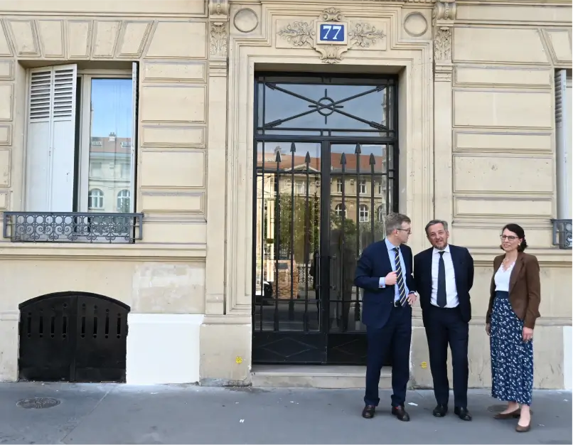 Trois gestionnaires de copropriété du cabinet Warren & Associés échangent devant la porte d'entrée en fer forgé d'un immeuble parisien en pierre de taille au numéro 77.